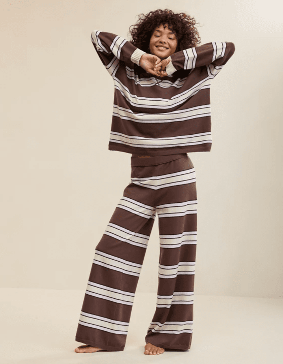 Person wearing a brown and white striped loungewear set, smiling with arms raised.