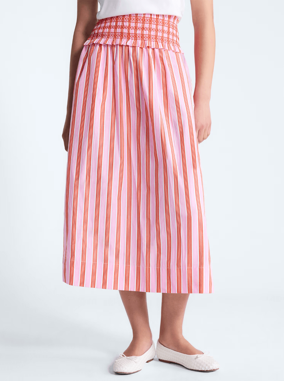 Person wearing a pink and orange striped skirt with white flat shoes.