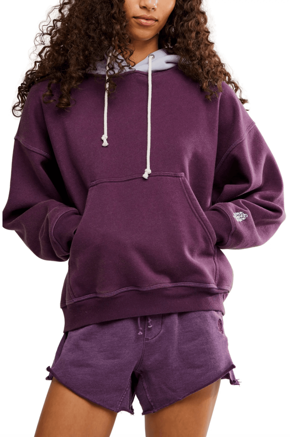 Person wearing a purple hoodie and shorts with hands in the hoodie pocket.