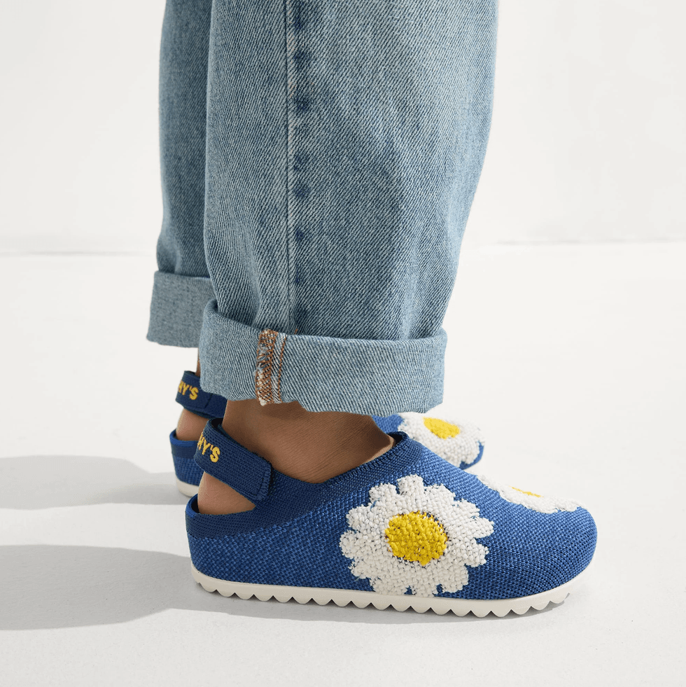 Person wearing blue shoes with daisy design and rolled-up jeans.