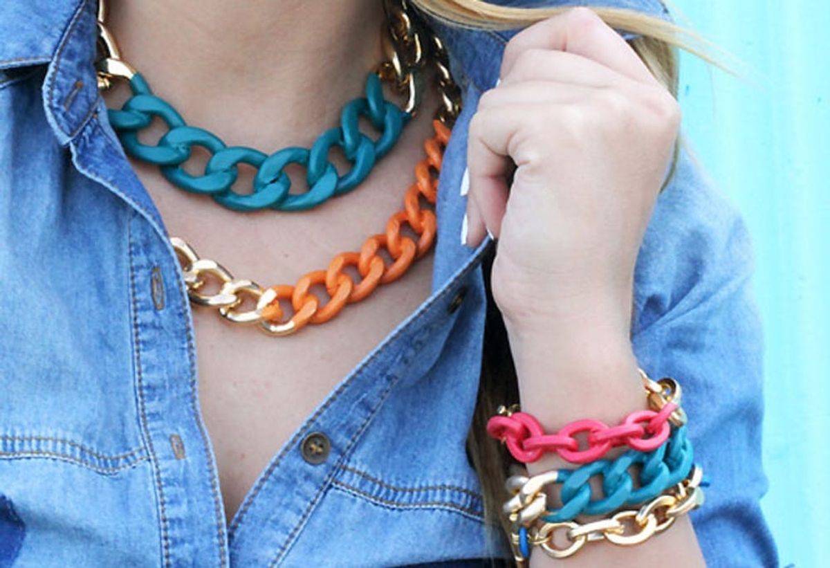 Person wearing chunky blue, orange, and gold necklaces with matching bracelets, in denim shirt.