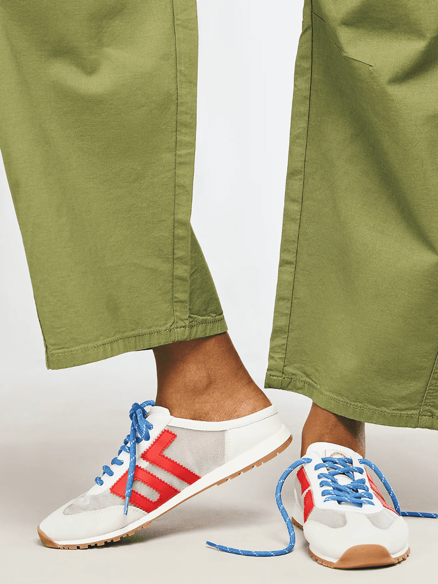 Person wearing green pants and white sneakers with red stripes and blue laces.