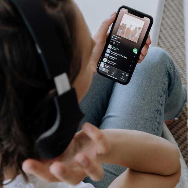Person wearing headphones, holding phone with music app open on screen.