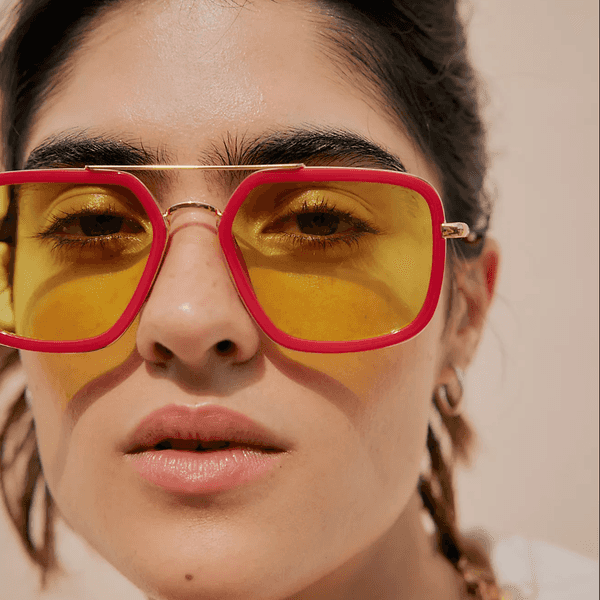 Person wearing large sunglasses with yellow lenses and red frames.