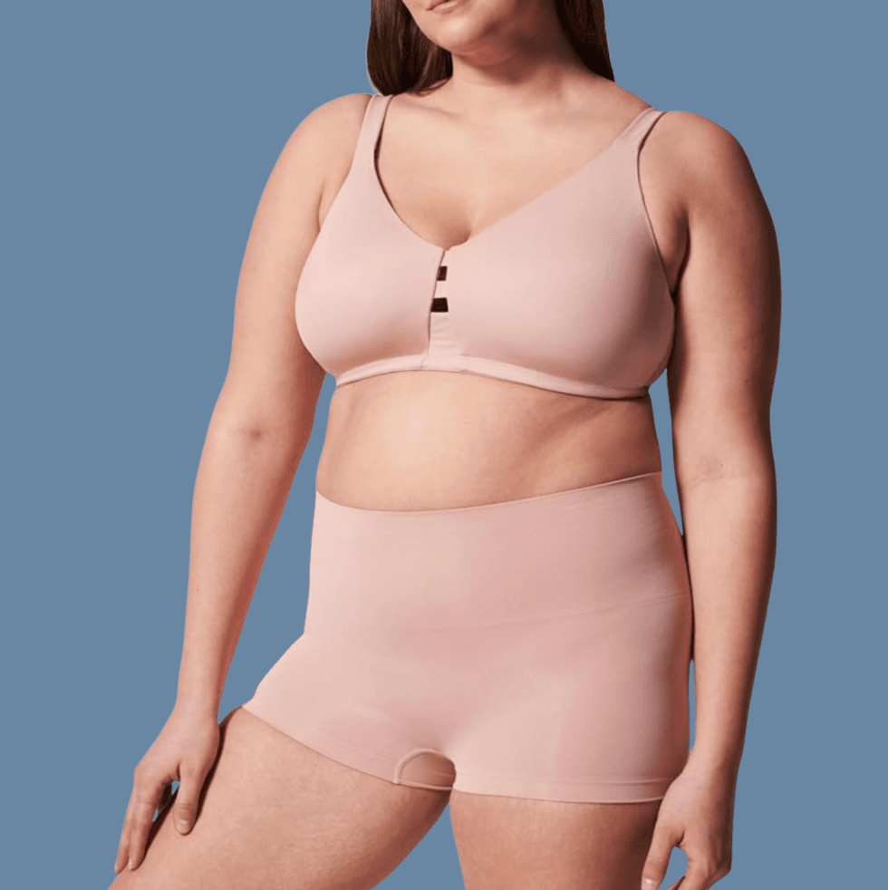 Person wearing nude-colored bra and high-waisted briefs, blue background.