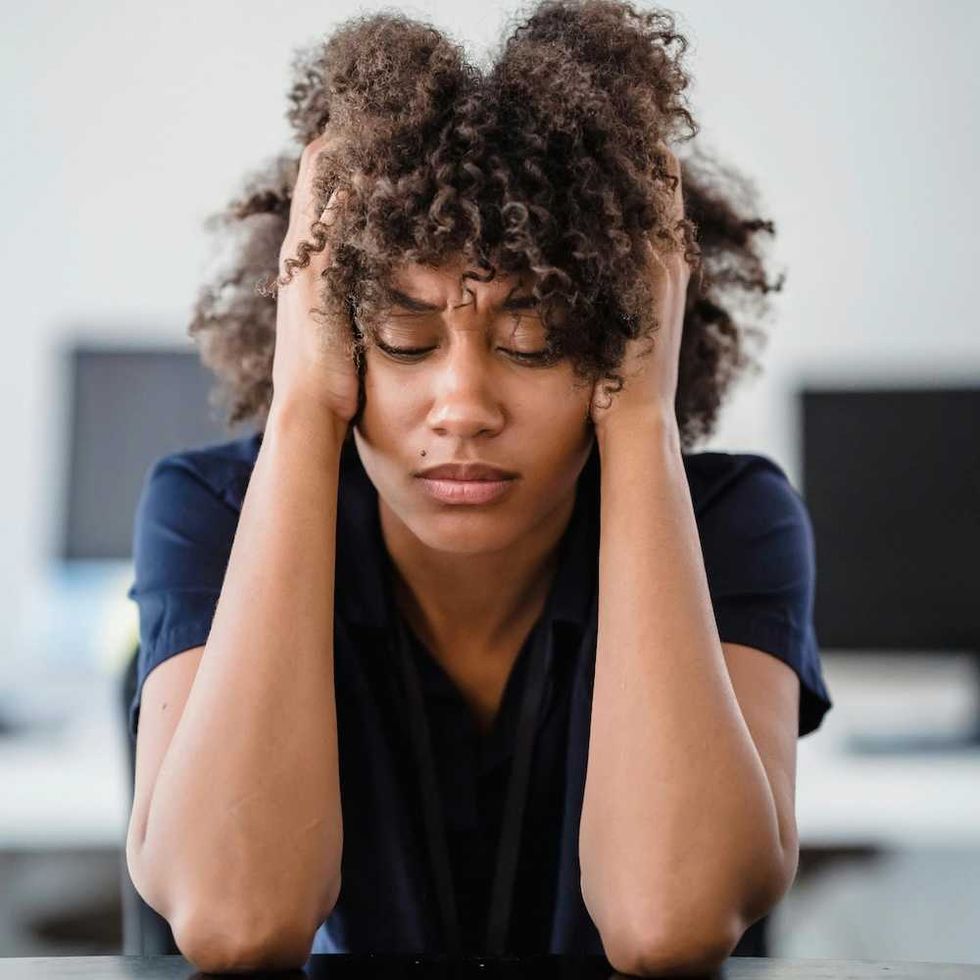 Person with curly hair, appearing stressed, holds head in hands at a desk.