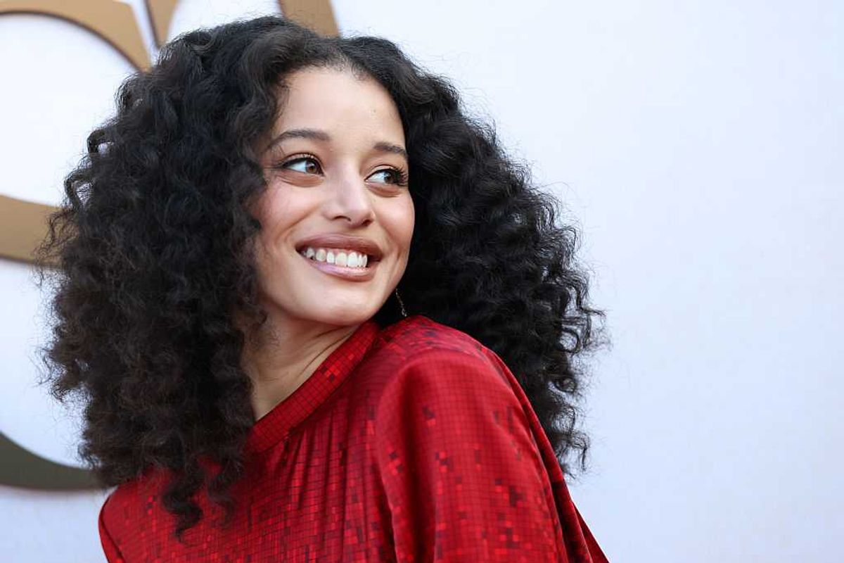 Person with curly hair smiling in a red outfit against a light background.