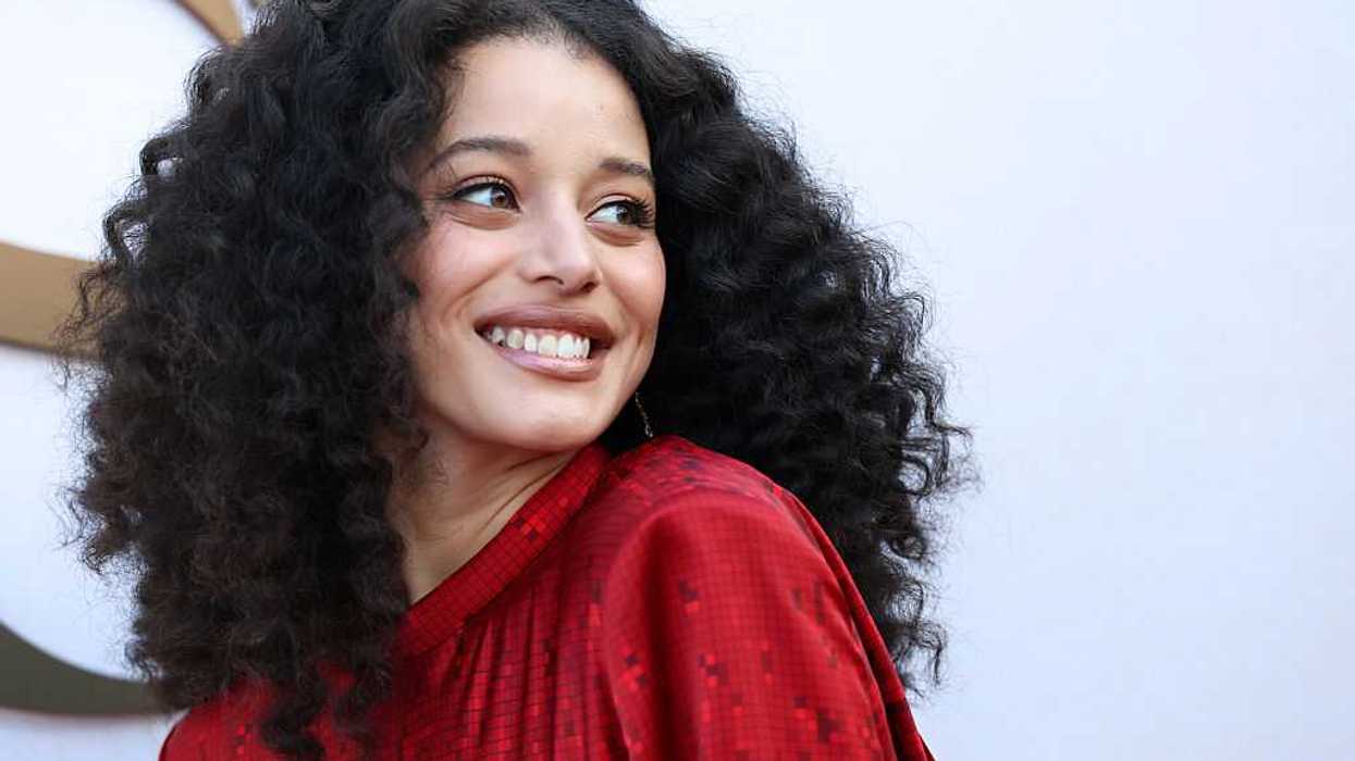 Person with curly hair smiling in a red outfit against a light background.