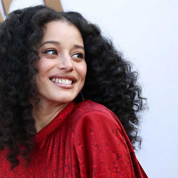 Person with curly hair smiling in a red outfit against a light background.