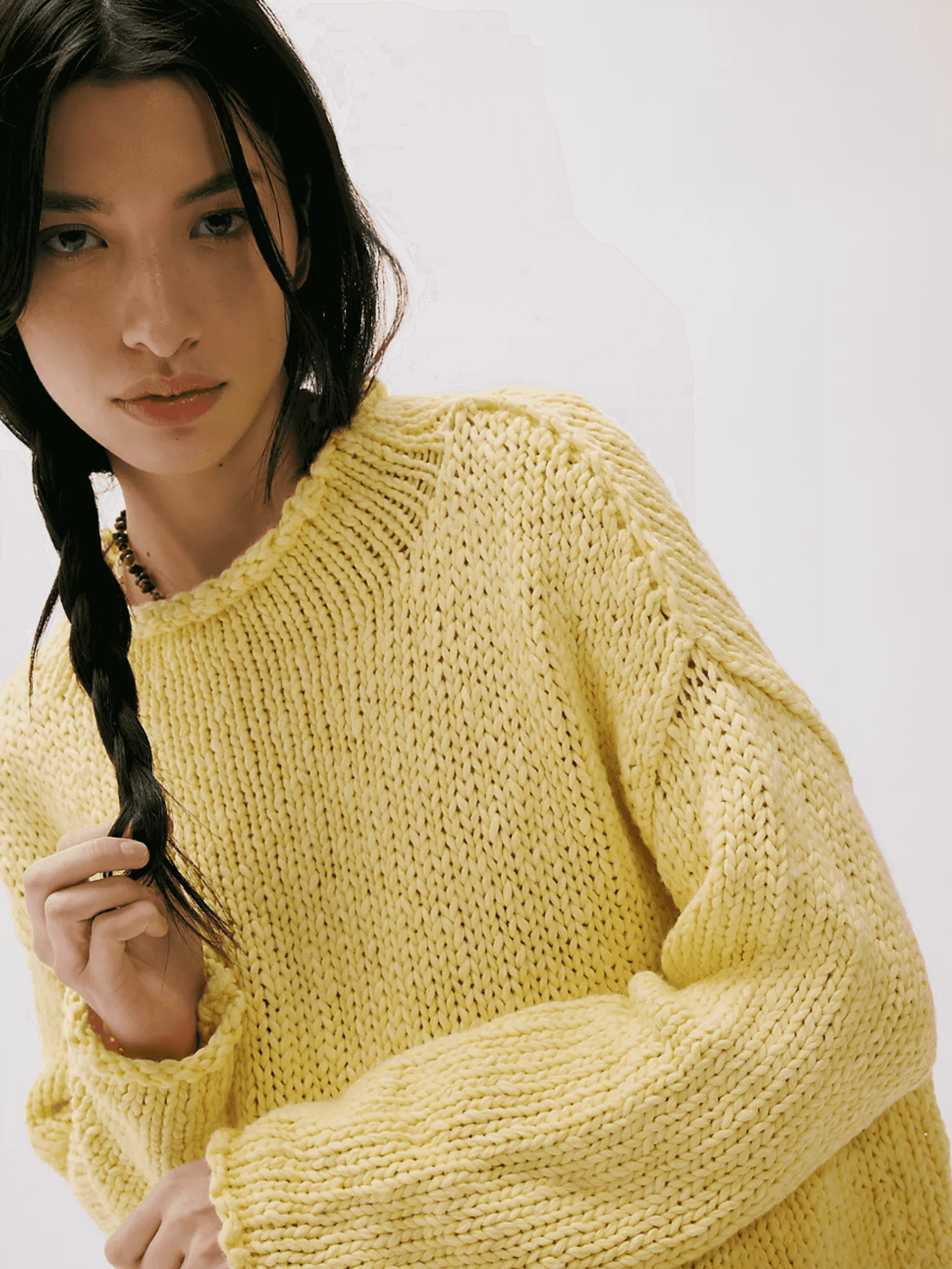 Person with dark hair in braid, wearing a chunky yellow sweater.