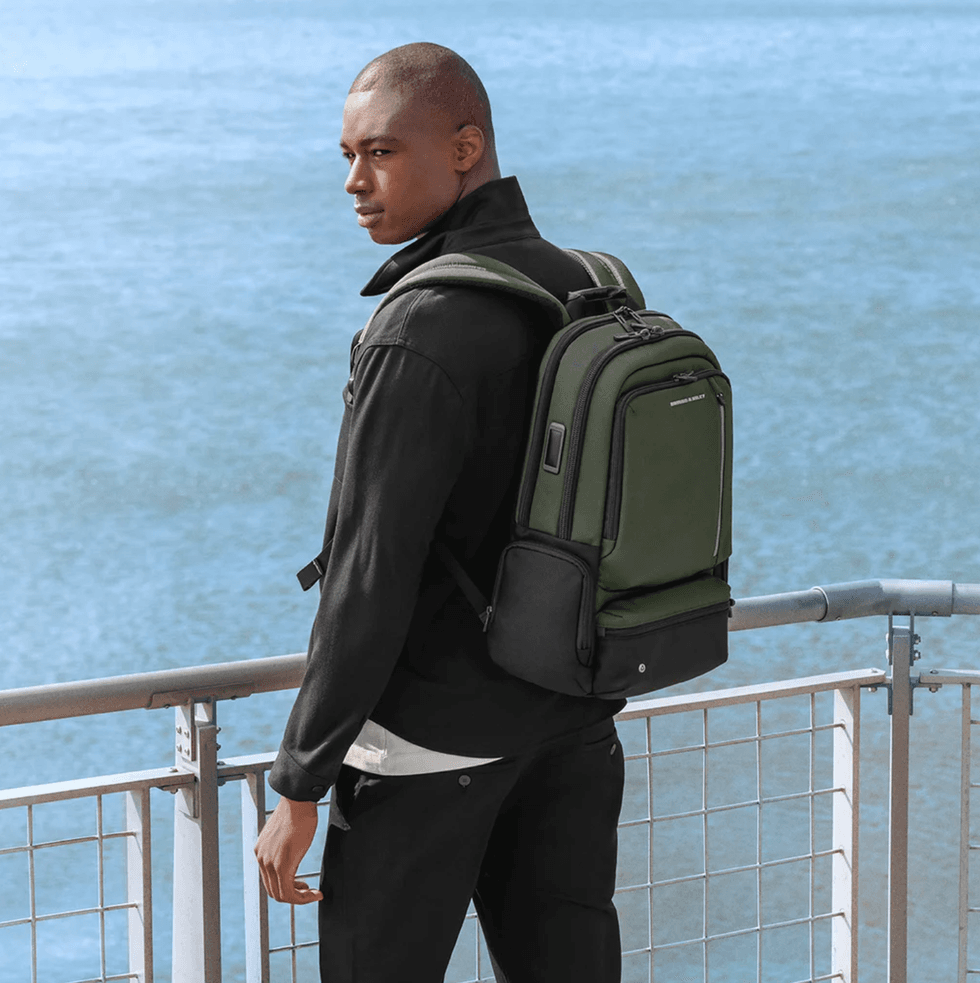 Person with green backpack standing by waterfront railing.