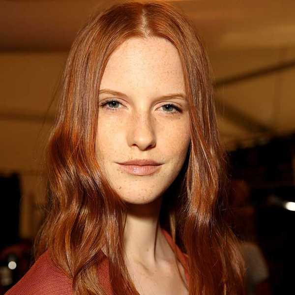 Person with long red hair and freckles, wearing a neutral expression indoors.