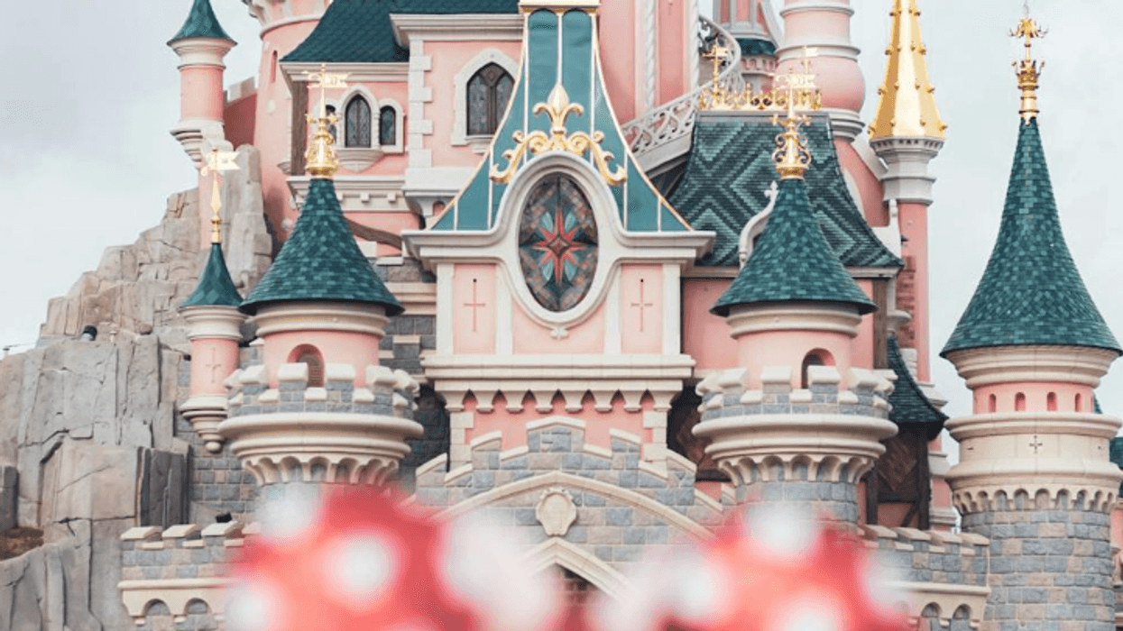Person with Minnie ears facing a whimsical castle surrounded by visitors.