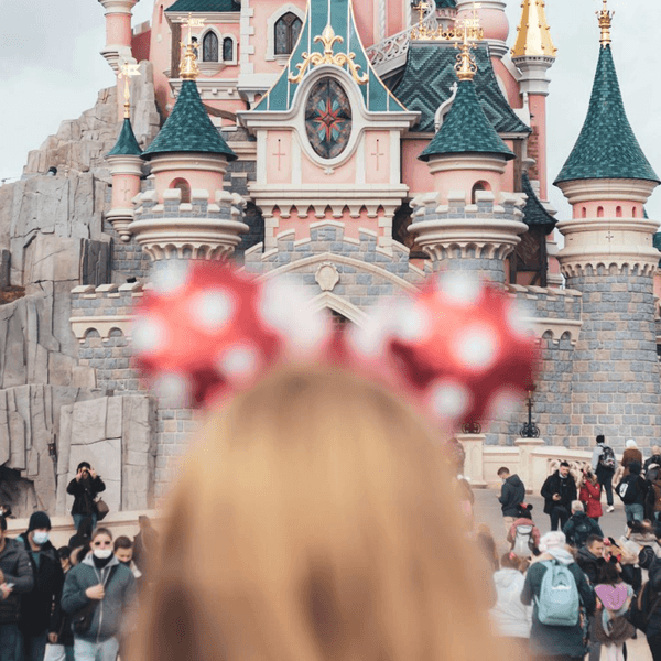 Person with Minnie ears facing a whimsical castle surrounded by visitors.