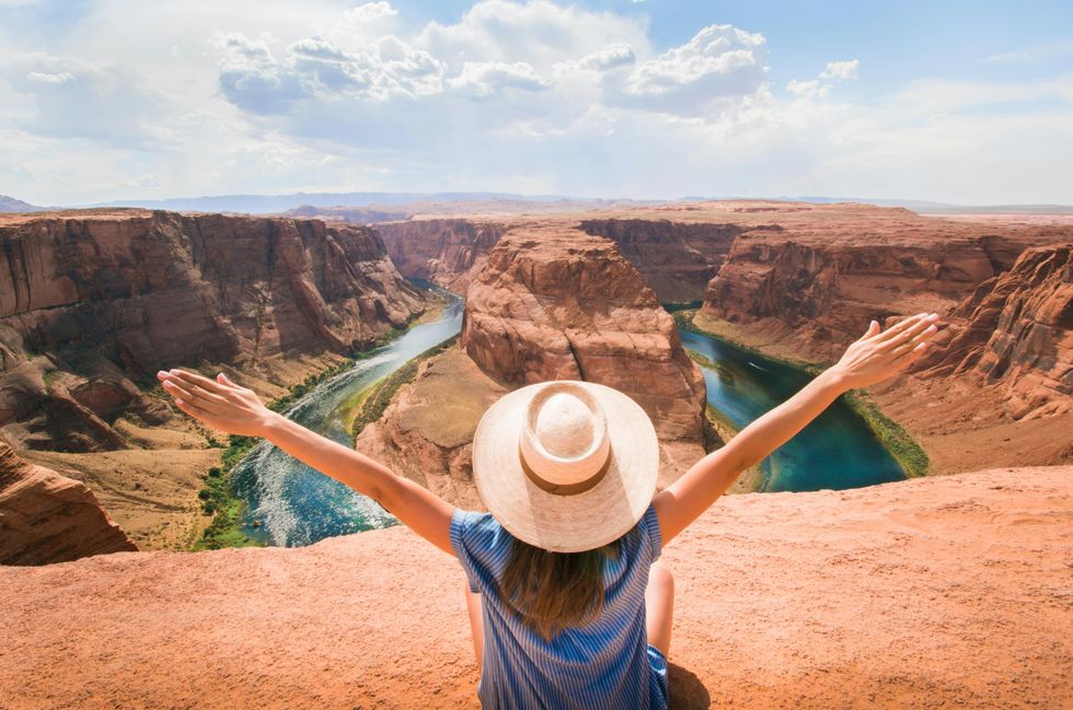 Person with outstretched arms overlooking river bend in a canyon, wearing a hat.