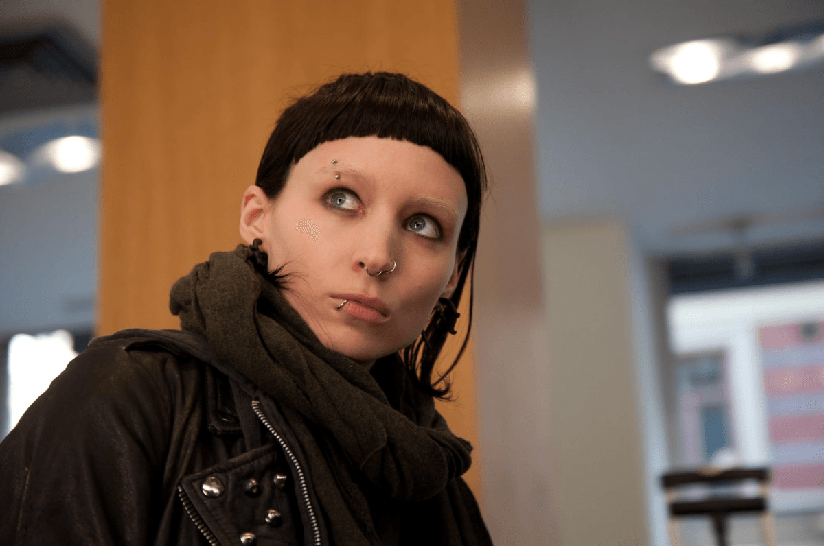 Person with piercings and dark attire looking to the side in an indoor setting.