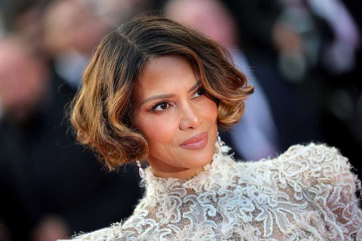 Person with wavy short hair in an elegant lace outfit, looking slightly to the side.