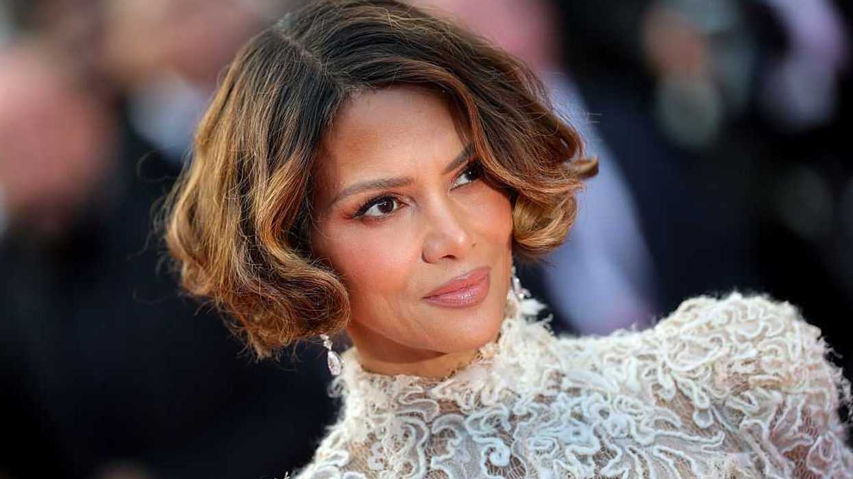 Person with wavy short hair in an elegant lace outfit, looking slightly to the side.