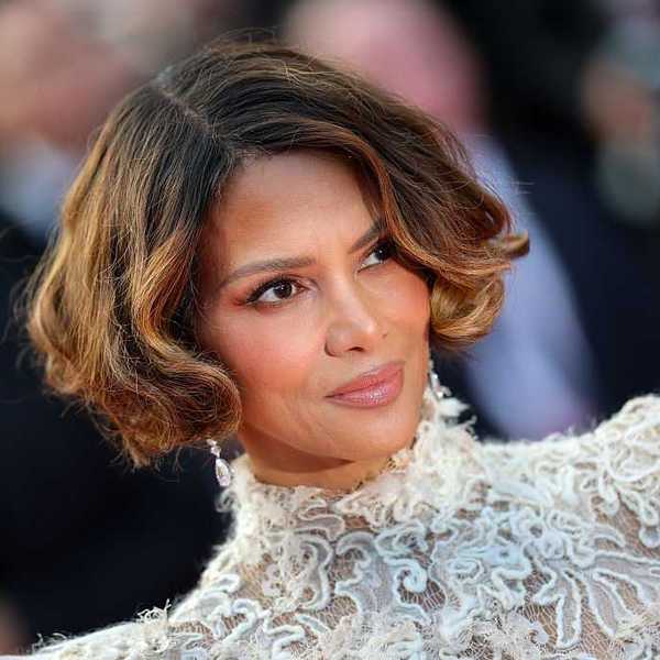 Person with wavy short hair in an elegant lace outfit, looking slightly to the side.