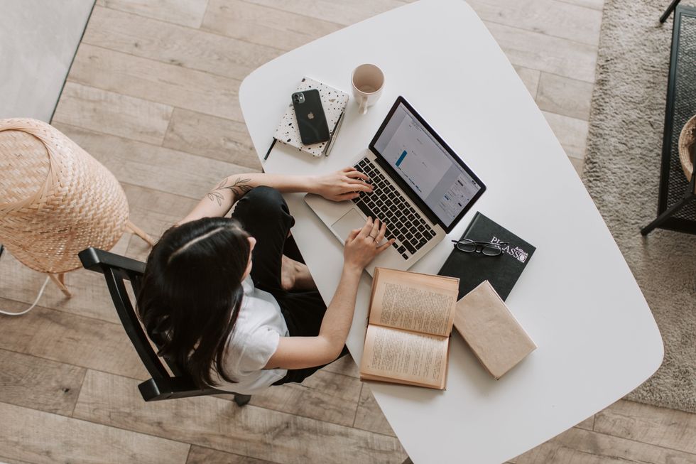 Person working on a laptop at a desk with books, notebooks, and a phone nearby.