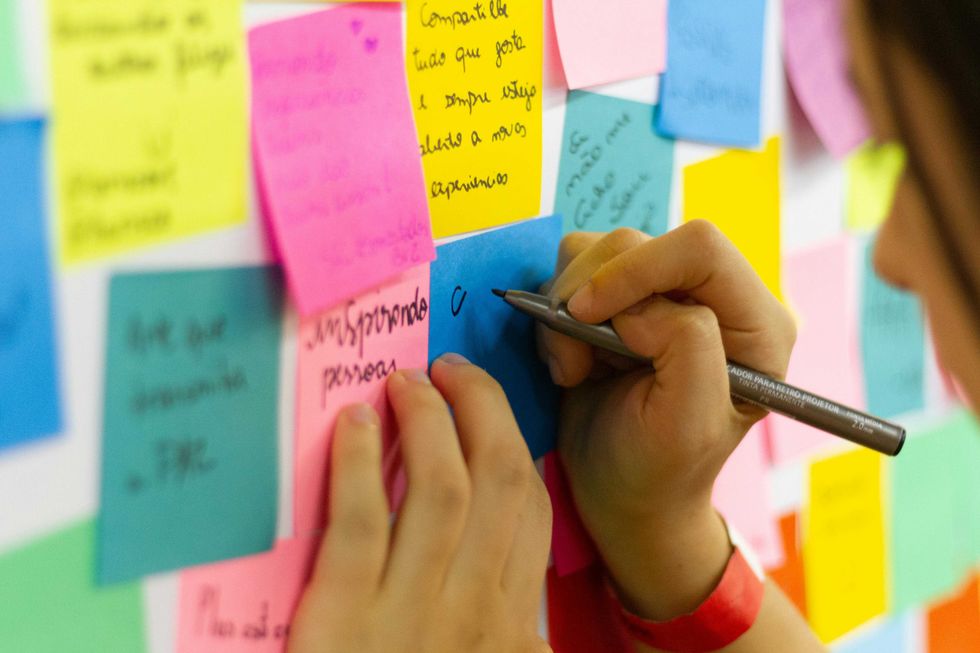 Person writing on colorful sticky notes on a wall.