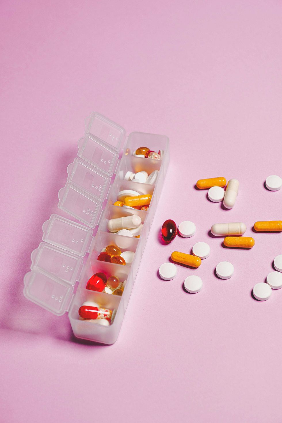 Pill organizer and scattered pills on a pink background.