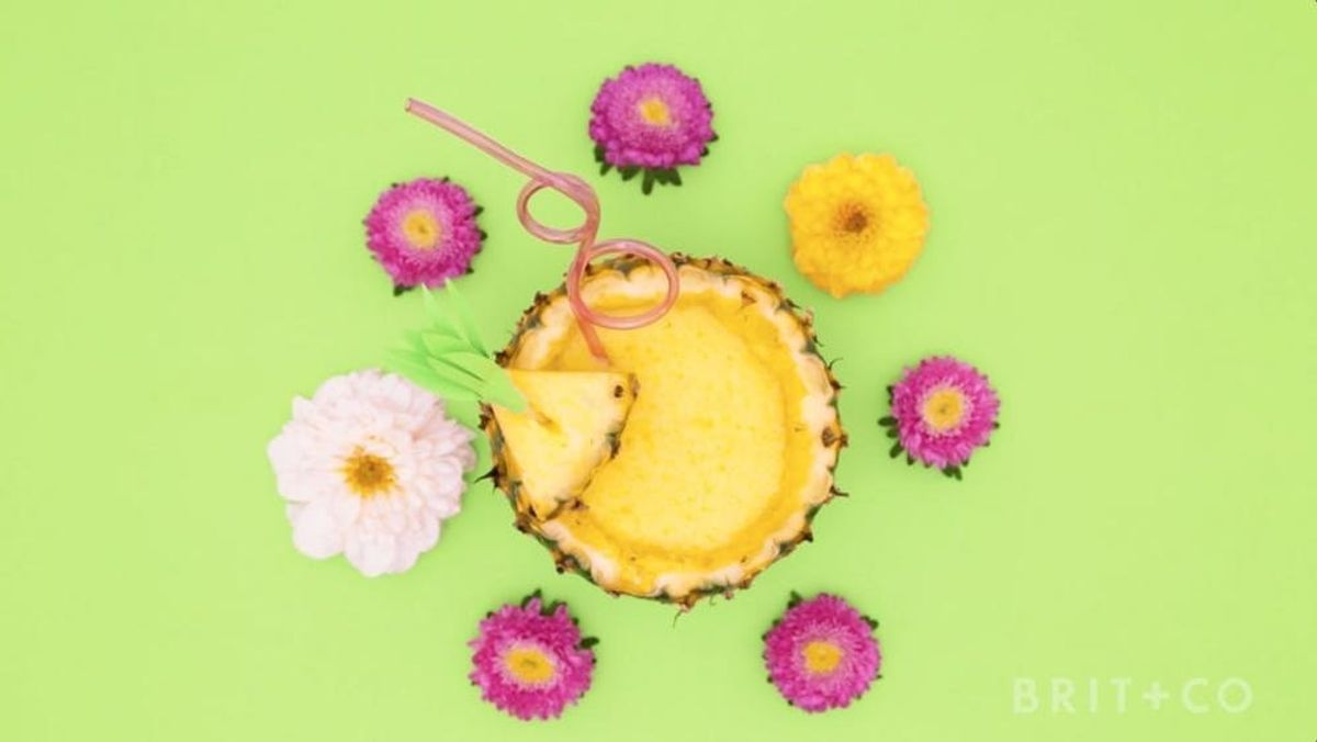 Pineapple Margarita with a straw and white and pink flowers around it on a lime green background