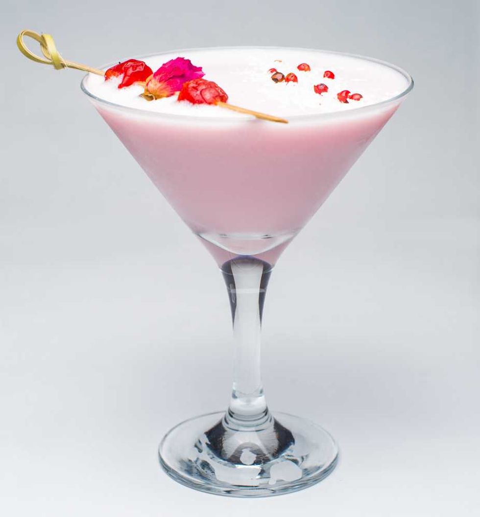 Pink cocktail in a martini glass, garnished with red berries and petals on a skewer.