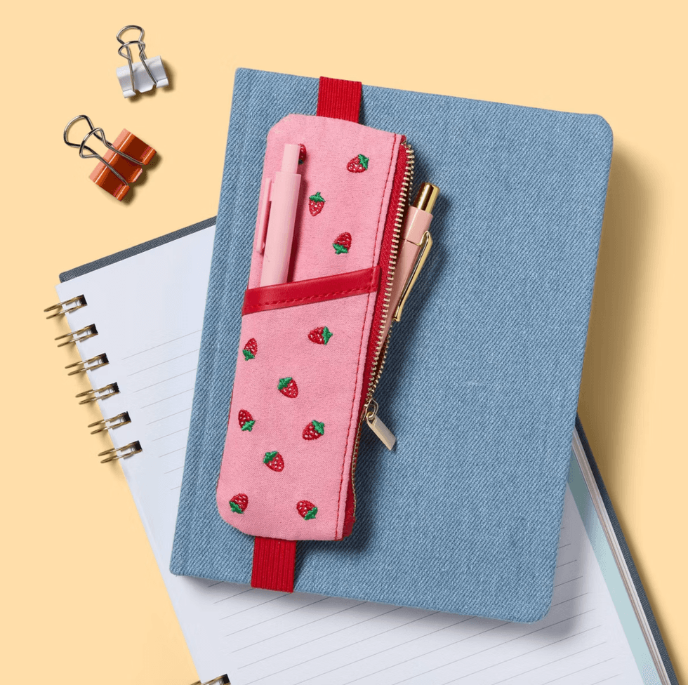 Pink strawberry pouch on a blue notebook, surrounded by binder clips and another notebook.