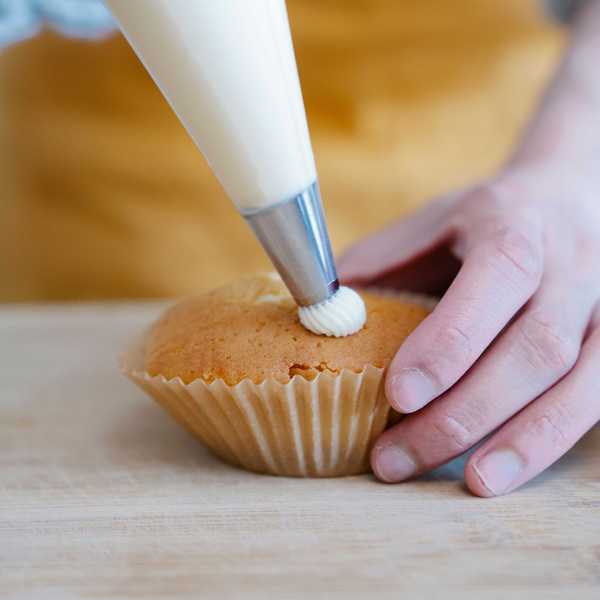 Piping cream onto a cupcake on a wooden surface.