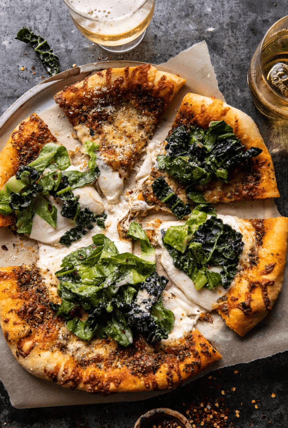 Pizza topped with kale and cheese on a plate with glasses of beer.