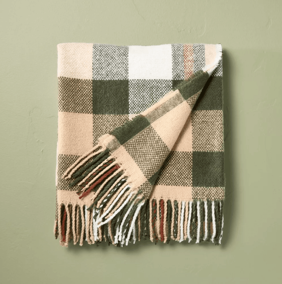 Plaid blanket with tassels on green wall.
