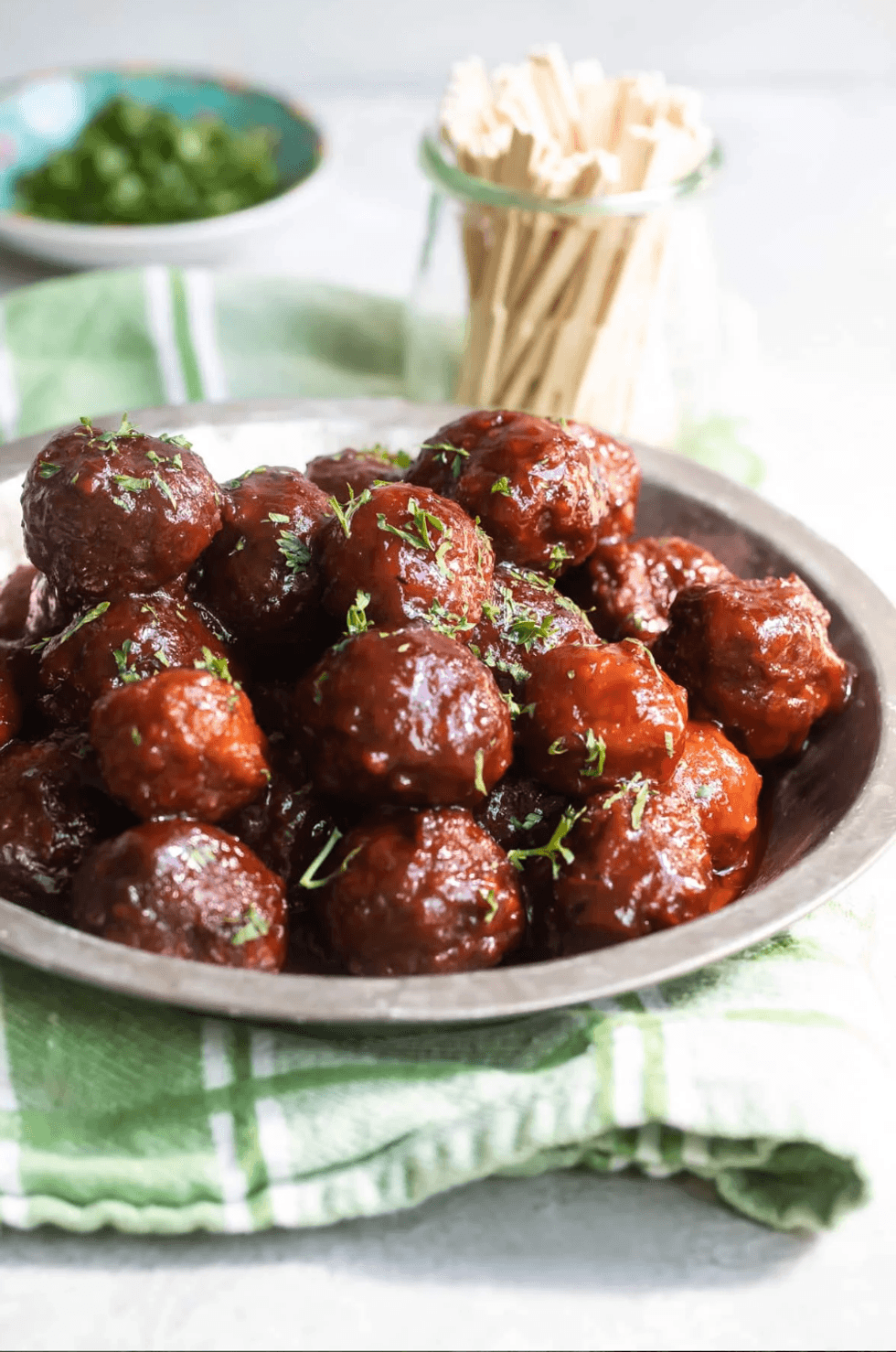 Plate of glazed meatballs garnished with herbs, beside toothpicks in a jar.