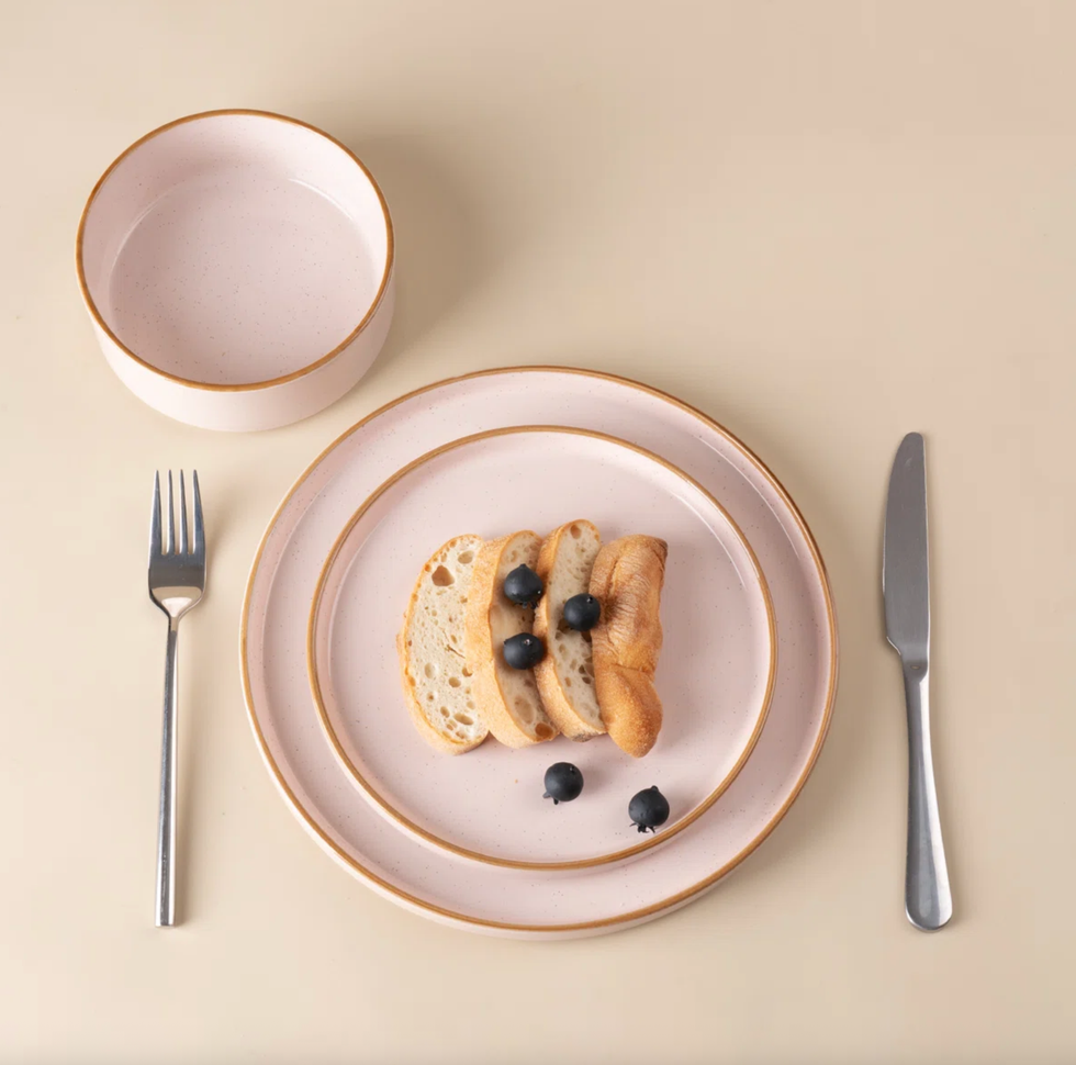 Plates with bread and berries, bowl, knife, and fork on beige surface.