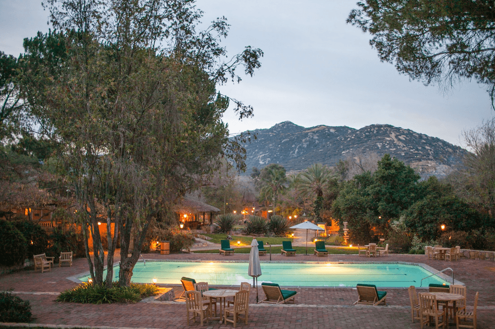 Poolside scene with chairs, trees, and mountains at dusk.