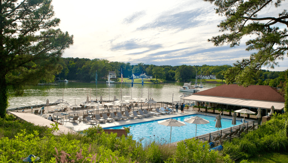 Poolside view with umbrellas by a scenic lake under a partly cloudy sky.