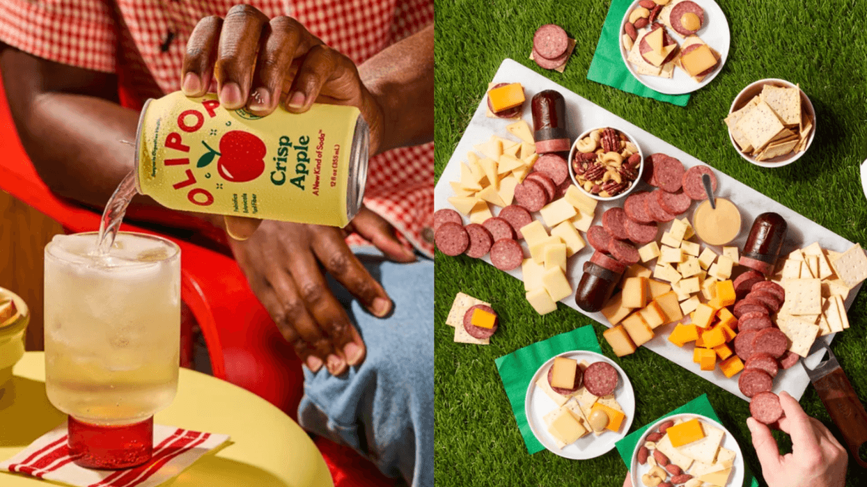 Pouring apple soda into a glass; cheese and sausage platter on grass.