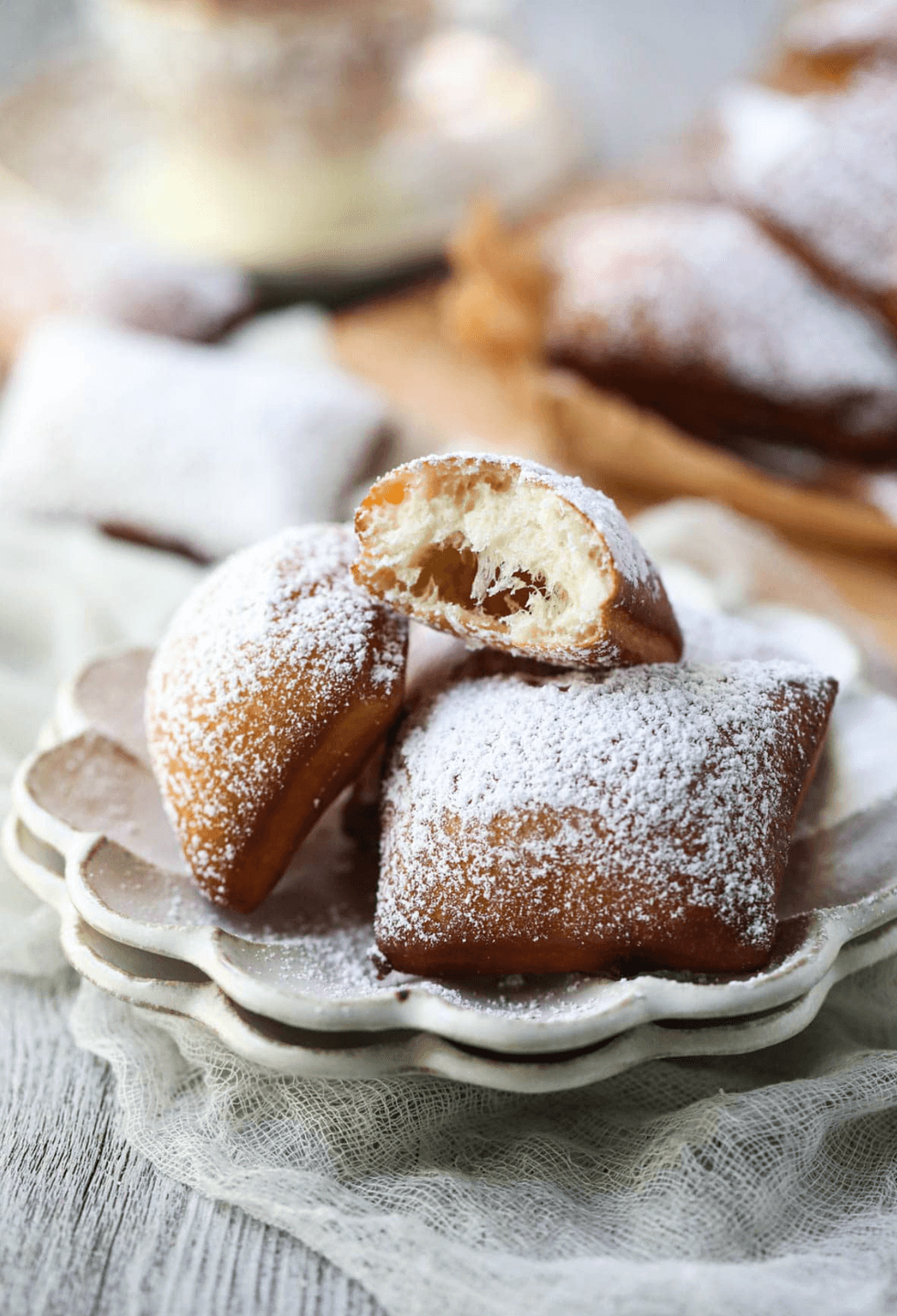 Powdered sugar beignets on a plate, one with a bite taken out.