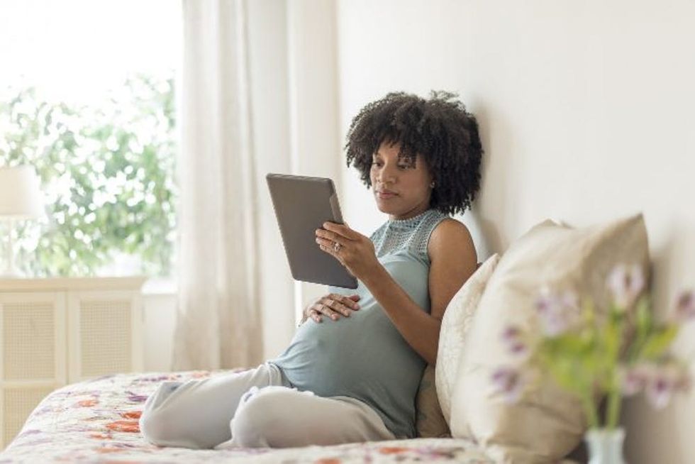 Pregnant African American mother using digital tablet in bed