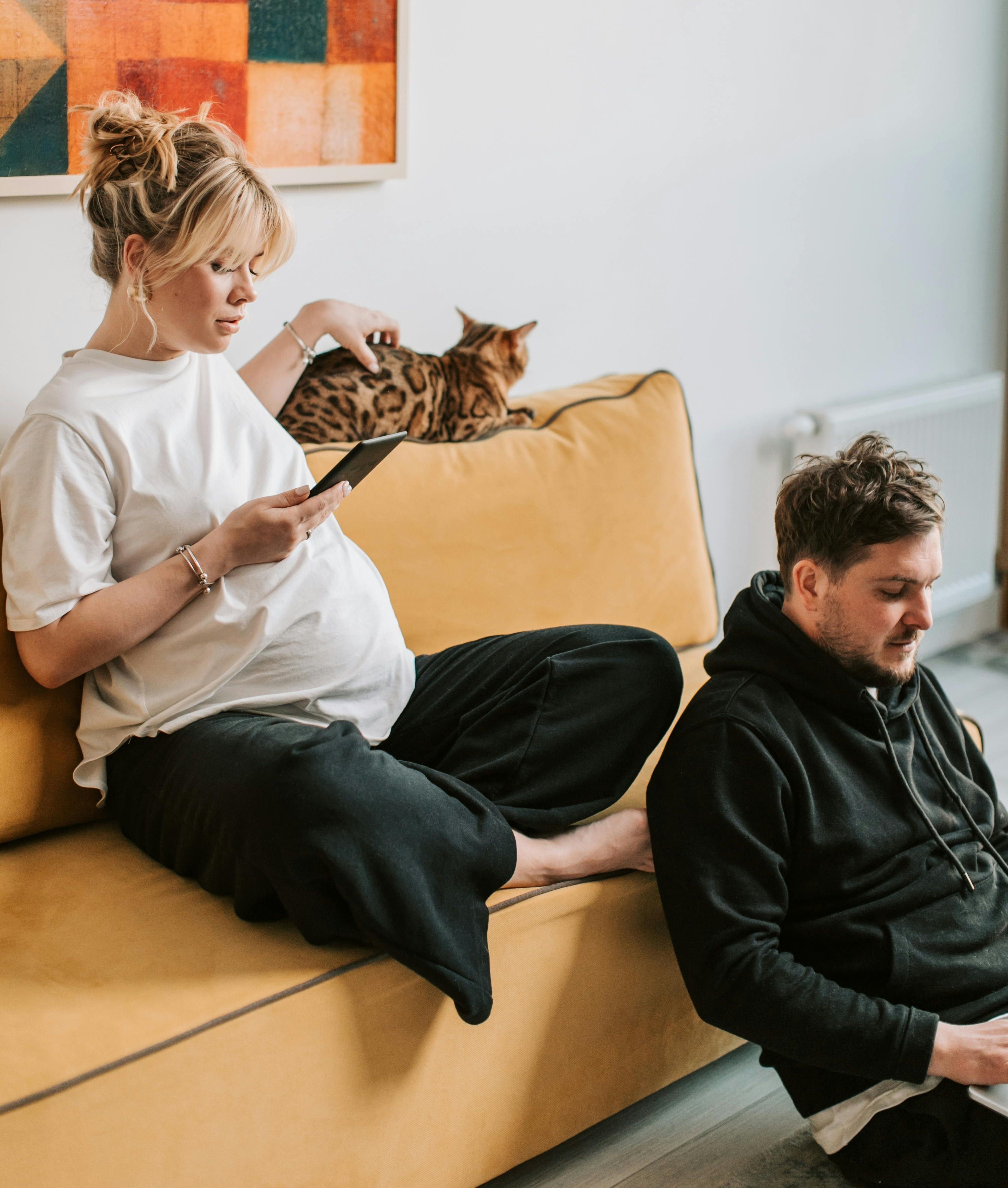 pregnant woman on her phone sitting on the couch with her cat and a man