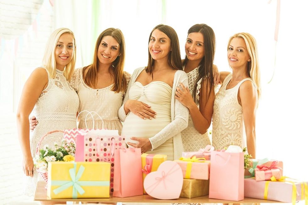 Pregnant woman with her female friends standing next to the table with baby shower presents.