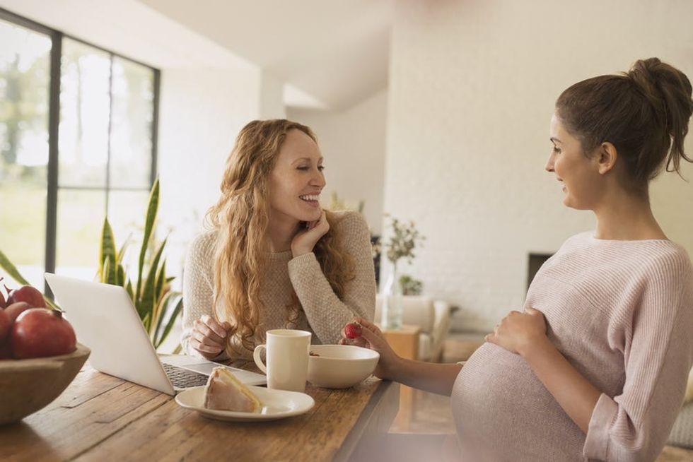 Pregnant women eating cake and fruit at laptop in dining room