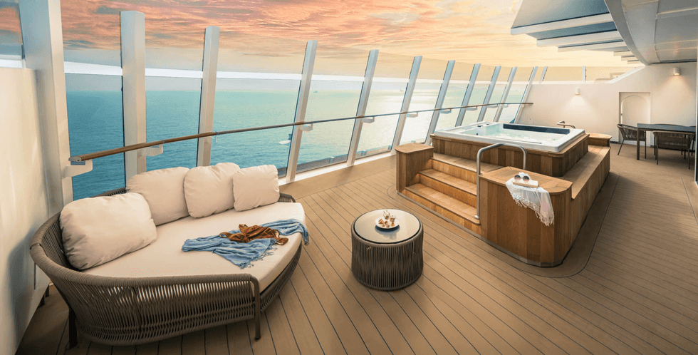 Private deck with a jacuzzi, lounge chairs, and ocean view at sunset.