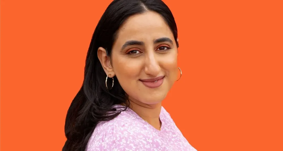 Priyanka Ganjoo smiles in front of an orange background.