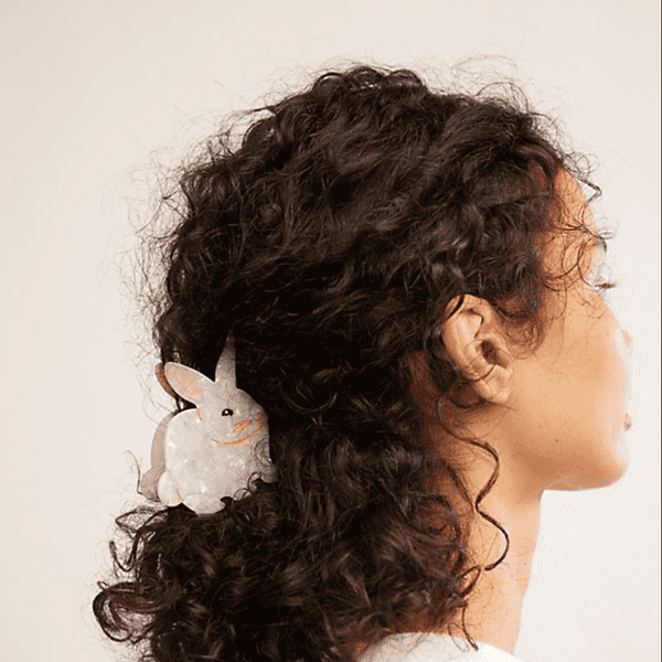 Profile of person with curly hair, rabbit-shaped hair clip, wearing a white shirt.