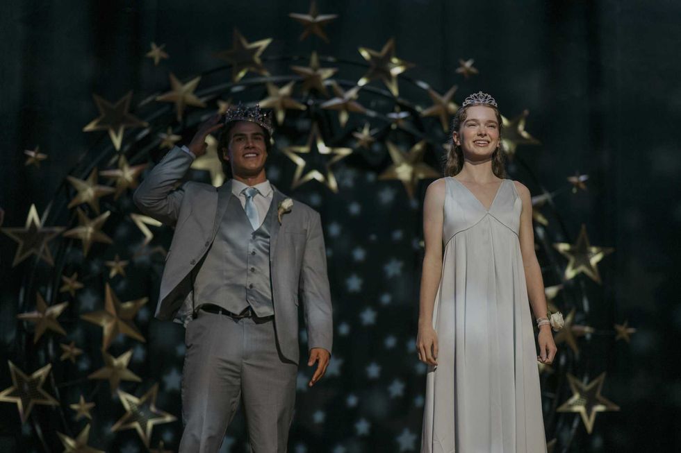 Prom king and queen smile under starry decor, wearing formal attire and crowns.