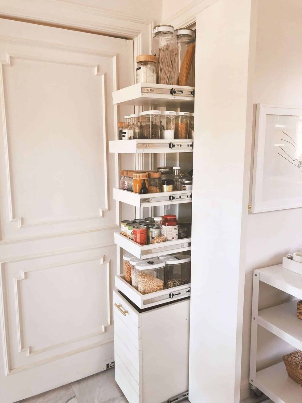 Pull-out pantry with neatly organized spices and jars in a white kitchen.