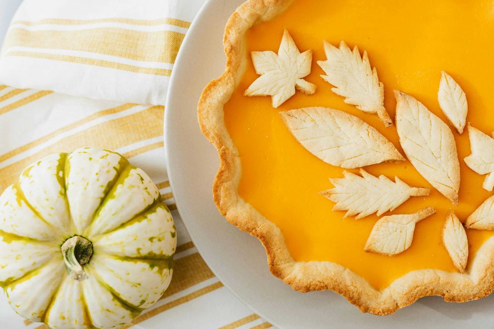 Pumpkin pie with leaf crust design and a small striped pumpkin on a striped cloth.
