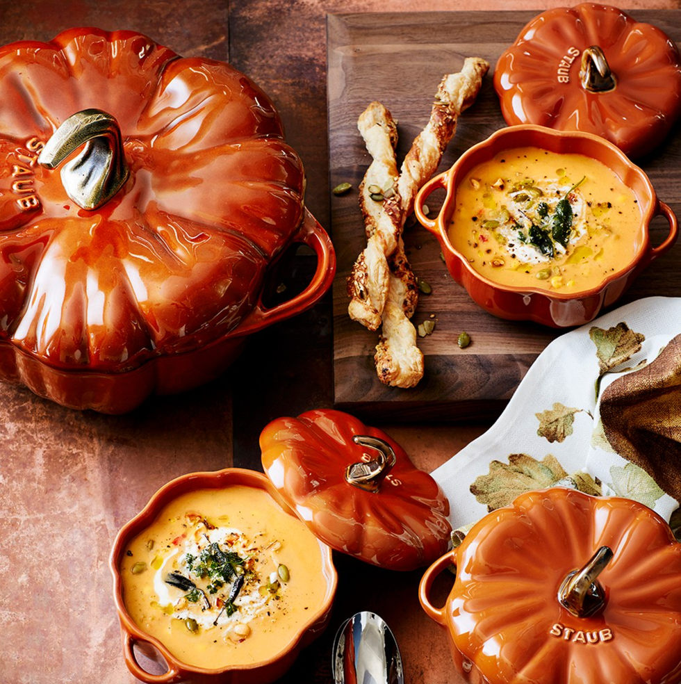 Pumpkin-shaped soup bowls filled with creamy soup, garnished with seeds and served with breadsticks.