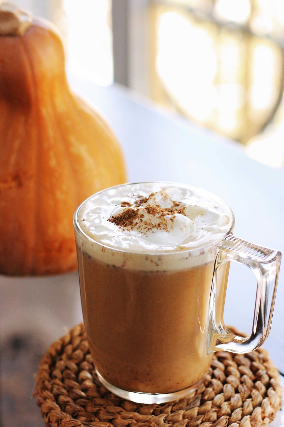 Pumpkin spice latte with whipped cream in a glass mug, beside a pumpkin.